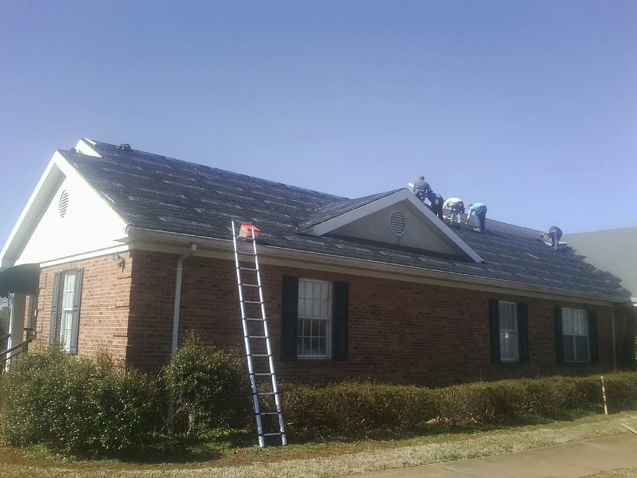 Crew tearing shingles off a brick ranch roof with a ladder set — Emergency Roof Repair work by our crew in North Easton