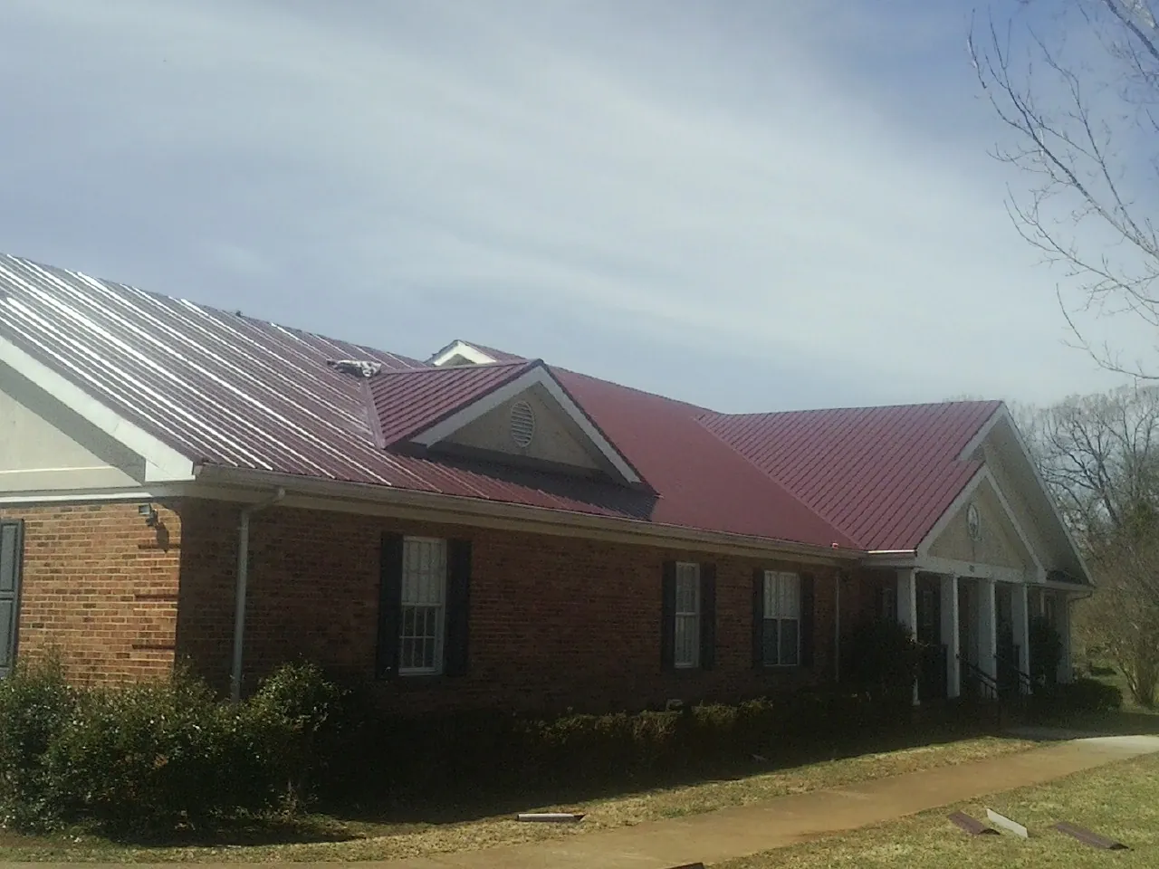 Red metal roof with gabled entries on a long brick building, from a Hail Damage Roof Repair job in North Easton