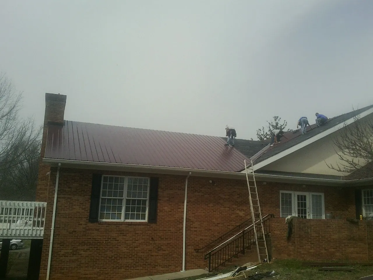Crew setting red metal roofing panels on a brick home in North Easton