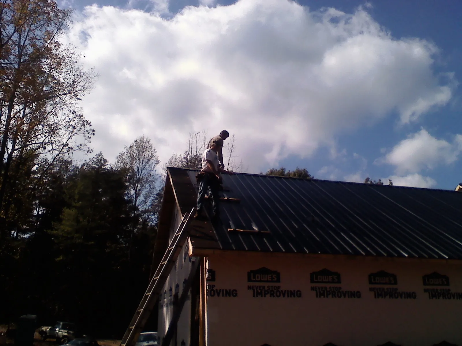 Roofer fastening dark metal panels high against a cloudy sky, from a Roof Inspection job in North Easton