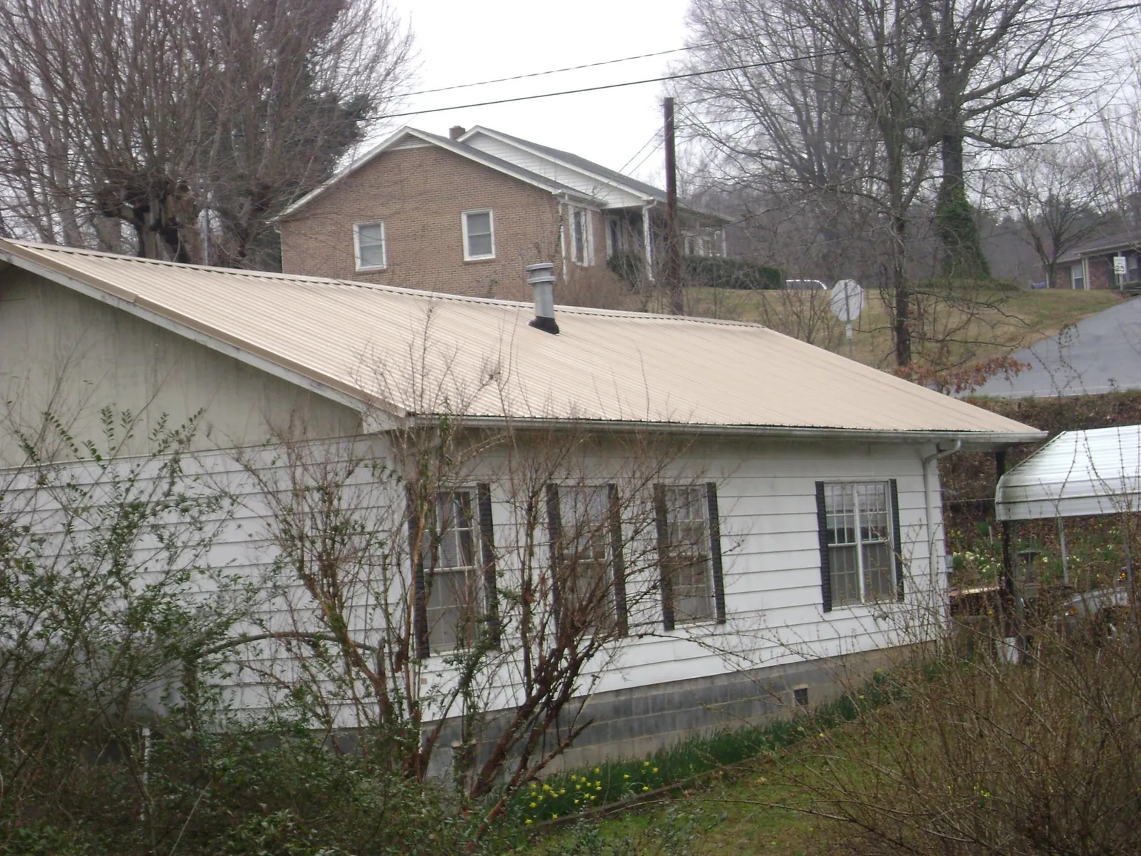 Tan metal roof on a white sided house set into a hillside — Commercial Roofing by Roofing Brothers in North Easton